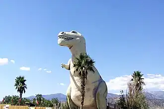 Large concrete Tyrannosaurus rex sculpture in a desert setting with mountains in the background
