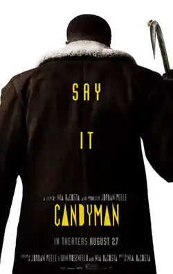 The Candyman faces opposite the viewer. On top of his large dark coat are the tagline and title "Say It" and "Candyman" in yellow font.