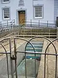 empty concrete baptismal pool with steps down into it and iron fence around