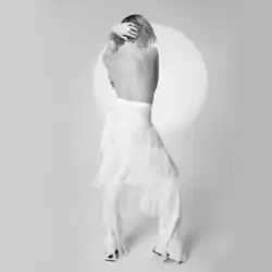 Black-and-white photograph of Carly Rae Jepsen from behind, topless in white fringe pants