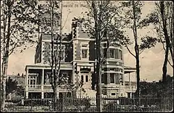 Monochrome photograph of a brick-clad residence featuring numerous architectural elements, including a turret imitating a castle.