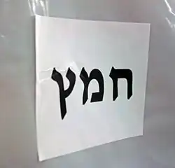 "Chametz" in large black Hebrew letters on a letter-size piece of paper, affixed horizontally to white plastic background.