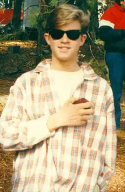 A male in a plaid shirt wearing sunglasses smiling toward a camera