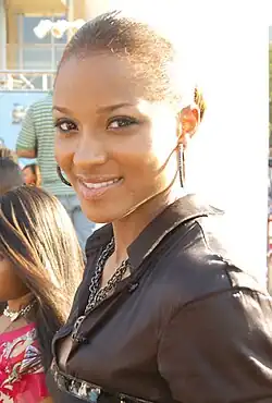 A young black woman in a dark leather jacket, smiling, with large, circular earrings.