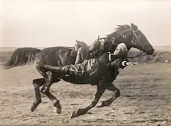 Picture of a man performing a trick pose while hanging to the side of a moving horse