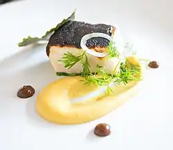 A slice of fish accompanied by a portion of pineapple puree and garnished with cilantro and onion.