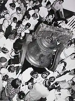 number of tourists, of all races and ages, dressed in the fashions of sixty years ago, gather around the Liberty Bell.
