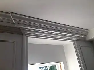 Crown molding may be a complex build-up of multiple trim elements, in this case built-out slightly above a window with short 90-degree returns