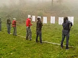 A line of people in front of targets reaching for their guns in holsters.