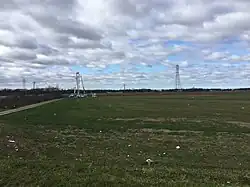 A field strewn with debris, with transmission towers in the background.