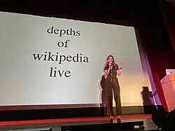 Rauwerda speaking at a live show in front of a slide with only the text "depths of wikipedia live".