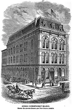 A lithograph of a four story building on the corner of two streets. It has tall, narrow arched windows in pairs with considerable decoration and a mansard roof. The stone street is busy with people, including a trolly partly out of frame and a two horse carriage.