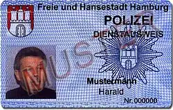 An identity card with a picture, the coat of arms of Hamburg, the police star of Hamburg and the German word sample written across.