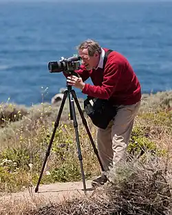 A photographer (Douglas Osheroff) setting up a shot with the aid of a tripod.