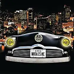 A city skyline at night is shown as the background. The front of a black-colored vehicle shows the headlines on, the band logo and a license plate with the song title on it.