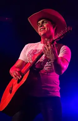 A young man wearing a white t-shirt and a cowboy hat, playing a guitar