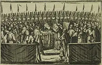 A man in a robe reads from a scroll surrounded by a crowd of people, all in conversation; behind them all are men astride horses, some of whom are bearing flags