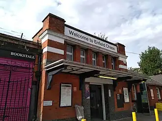A two-story thin red-brick building with a flat roof. The first floor has a doorway with a canopy above; the second floor has five windows; above the second floor is a large sign that reads "Welcome to Enfield Chase".