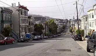 Eureka Valley, looking north on Castro Street from 20th. The giant rainbow flag at Castro and Market is just visible. In the summer months, fog tends to roll in over Twin Peaks and other hills to the west in the evenings and retreat again the next morning.