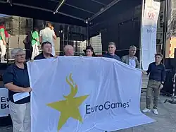 multiple officials holding a EuroGames flag at the stage