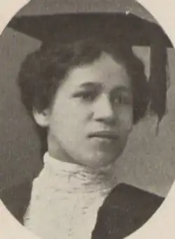 A young Black woman with light skin, wearing an academic cap and a white blouse with a high collar