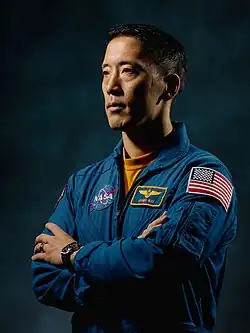 NASA astronaut Jonny Kim, an Asian man in a blue flight suit, is in front of a dark background.