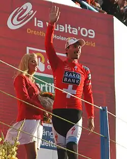 A man walking across a stage while waving and wearing a red jersey