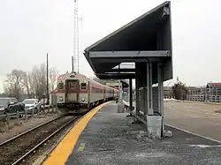 A passenger train at a low-level railway platform with an angular shelter