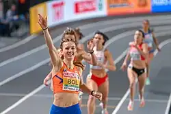 Photo of Femke Bol in the center raising her right hand, with other contestants blurred in the background