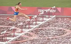 Photo of Femke Bol while jumping over a hurdle on a red athletics track