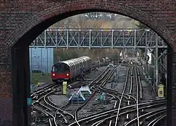 A view through a red-brick archway of a bridge. A complex of railway tracks interconnected with points is in the foreground with a train in the distance