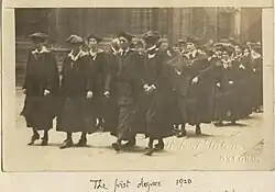 Black and white image of women wearing graduation robes, on their way to the degree conferral ceremony