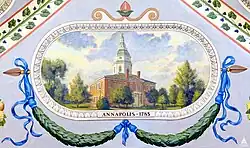 A painting showing downtown Annapolis, Maryland. A church building is in the center of the image, surrounded by trees, and a green garland adorned with blue ribbons sits below it. Text directly under the church painting says "ANNAPOLIS, 1783".