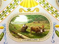 Two settlers use a team of oxen to remove the stumps of newly felled trees while, in the background, others build a log hut next to an inland river.