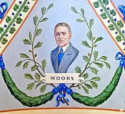 A painting depicting a portrait of Elliott Woods. He is wearing a grey suit with a blue tie, and is looking directly forward. Behind him are green garlands and plants, and directly under him is the text "WOODS".