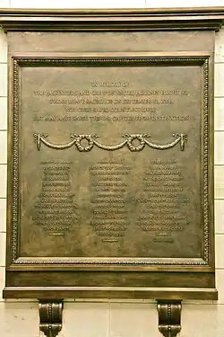 A gold bronze plaque with the names of passengers of United Airlines Flight 93. In the middle of the plaque is an engraved garland that loops twice.