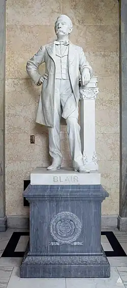 A white marble statue of Francis Preston Blair. His left arm is resting on a pillar, and he had his right hand on his hip. He is wearing an overcoat, and on the cap of the pedestal is the word "BLAIR" engraved in gold.