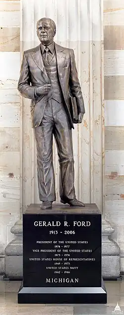 The statue depicts Ford wearing a three-piece suit and leaning forward, his feet splayed and his slightly raised left heel suggesting forward motion; the sculptor stated that this posture is "meant to embody the idea of someone standing up to serve their country when called." The president's right hand holds his open suit jacket with two fingers below the right lapel and his left hand holds two thick files, the outer one of which carries the presidential seal. On the pedestal, text reads: "GERALD R. FORD, 1913-2006, MICHIGAN".