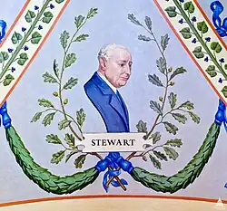 A painting depicting a portrait of J. George Steward. He is wearing a blue suit, and is looking to the right. Under him are green garlands and plants, and directly under him is the text "STEWART".