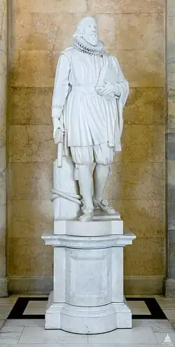 A white marble statue of John Winthrop. He is holding a rod in his right hand, and has his left hand up to his chest. He has a frilled collar and traditional Victorian clothing, and the pedestal is made of the same white marble material.