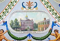 A brown brick building surrounded by trees and other building. Below the building are green garlands with blue ribbons, and directly under the building are the words "PHILADELPHIA, 1774".