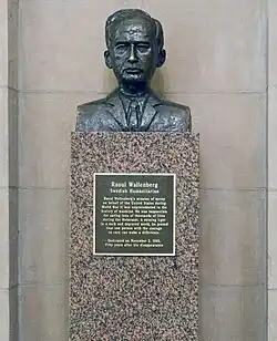 A brown bronze bust of Raoul Wallenberg. He is wearing a suit and tie. On the granite pedestal is a black-and-gold plaque.