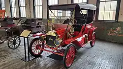 A red-colored, old-fashioned car with four seats and brass fittings