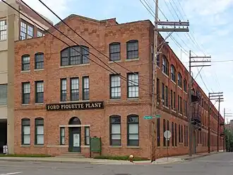 A three-story brick building with late Victorian-style architecture. A row of telephone poles are on the right and a historical marker is next to the front door.