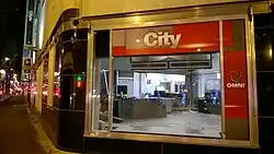 A studio partially disassembled, seen through the large picture window on the corner of the Hudson's Bay Building. City and Omni signage is seen near the window.