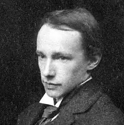 A greyscale photograph of G. E. Moore, wearing formal clothing and smoking with a tobacco pipe.