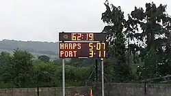 Scoreboard at a GAA match. Spectators are expected to calculate the total score themselves: Harps have scored 5 goals and 7 points (total 22), while Port have 3 goals and 11 points (total 20).