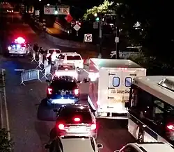 vehicular traffic merging lanes in front of a police checkpoint on Queensboro Plaza right before the Queensboro Bridge, which crosses into Manhattan; metal barriers reducing the roadway to one lane; police officers speaking to drivers before allowing passage; police cruisers nearby