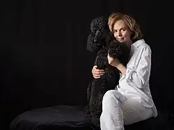 Georgina Montagu wearing white trousers and shirt with her previous black standard poodle Albert