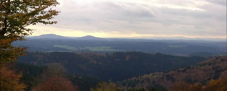 View of the Gleichberge (679 and 641 m), 24&nbsp;km away. Right in the background is the High Rhön with the 928-m-high Kreuzberg 67&nbsp;km away, immediately in front (centre half right) the 7-km-distant Ratscher Bergsee. In the foreground is the 621-m-high, Wachberg, 3&nbsp;km away